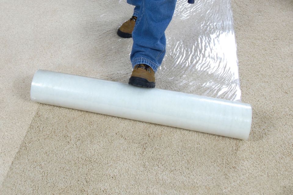 A man stands on a carpet with a roll of plastic, symbolizing a protection service based in San Jose, CA.