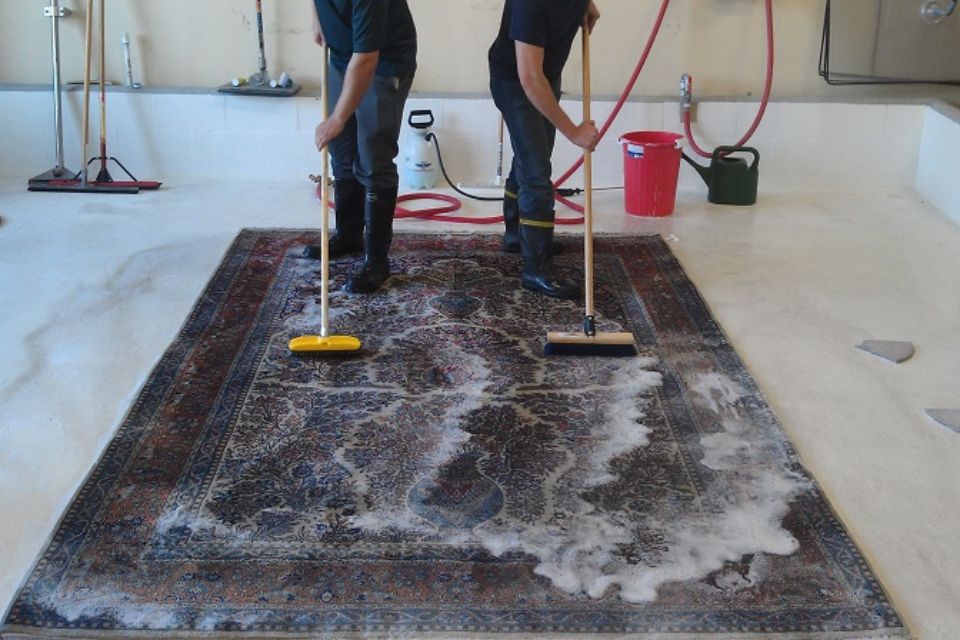 Two men vacuuming an area rug as part of a cleaning service in San Jose, CA.