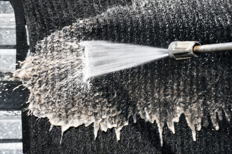 A person cleans a black cloth using a hose, demonstrating a carpet cleaning technique.