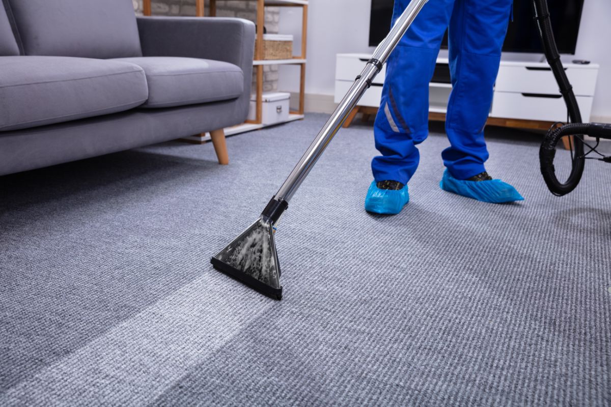 A person using a vacuum cleaner to clean a carpet, demonstrating effective carpet cleaning techniques.