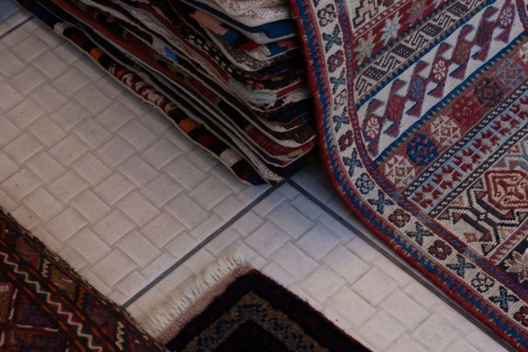 A pile of various rugs on the floor, showcasing the best indoor carpet materials for home decor.